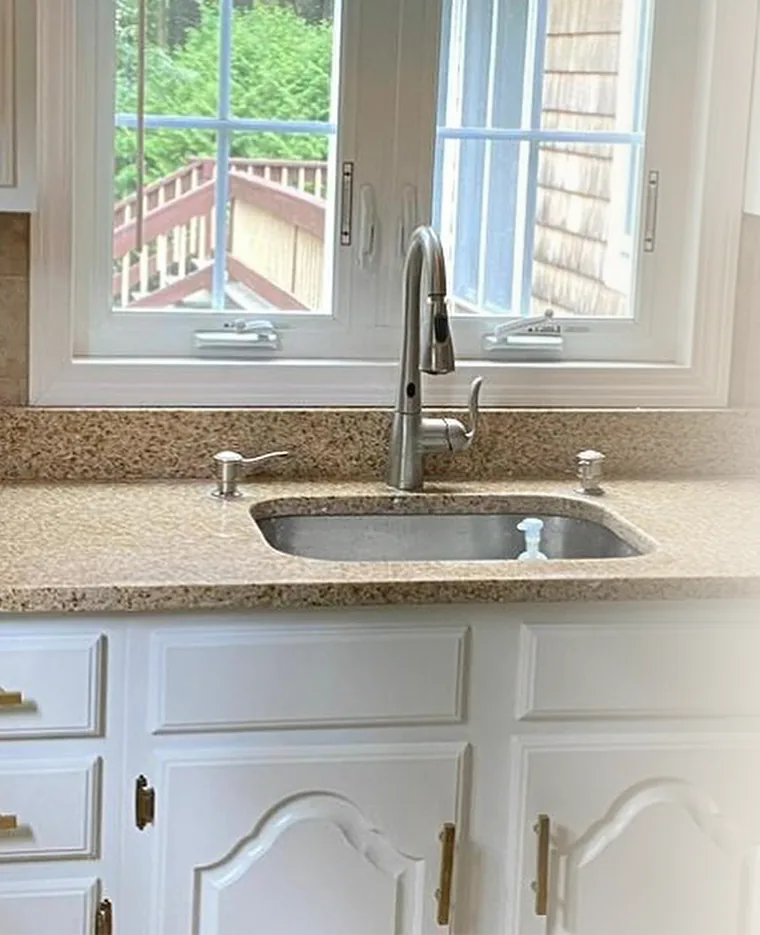 Kitchen sink under a window with white cabinets and stone countertop